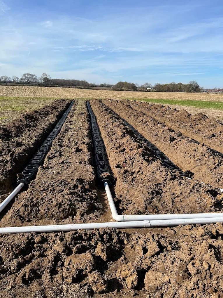 Three parallel leach field lateral lines of perforated pipe laid in open trenches with PVC distribution header across the front