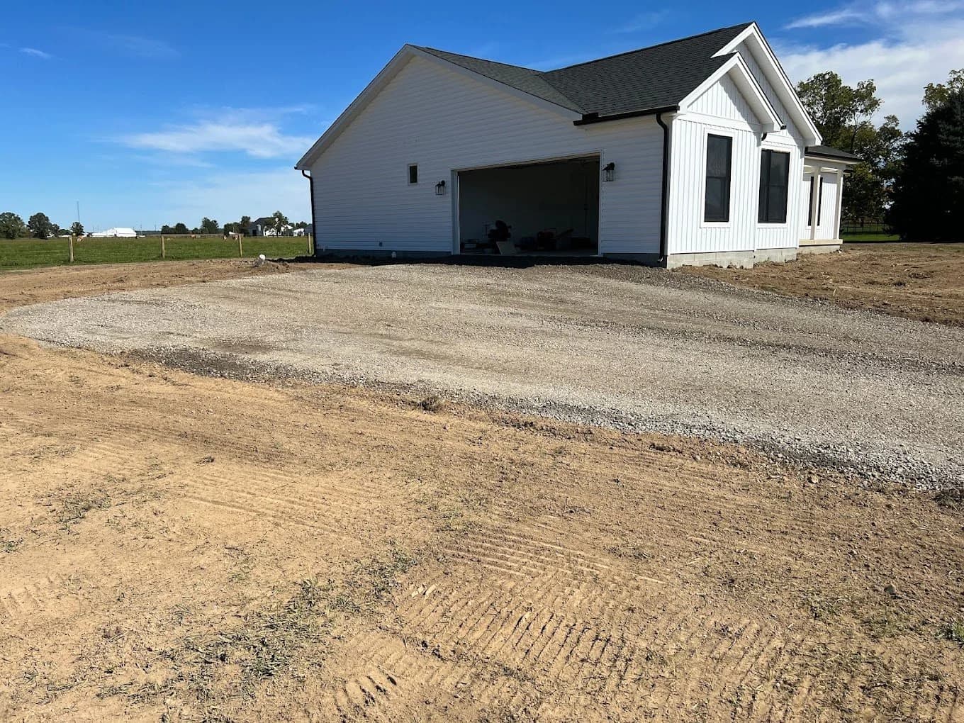 Finished compacted gravel driveway and turnaround in front of a new white farmhouse with an attached garage