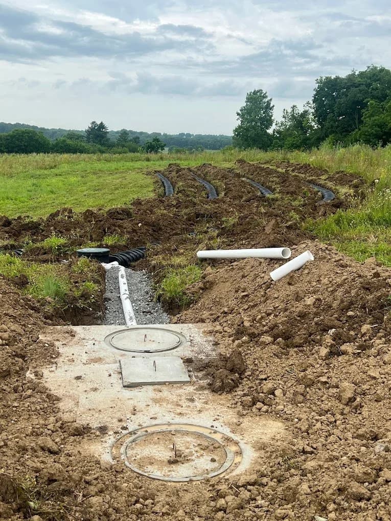 Completed septic system with two concrete tank lids at grade and curved leach field lines running across a hillside pasture in rolling Ohio countryside
